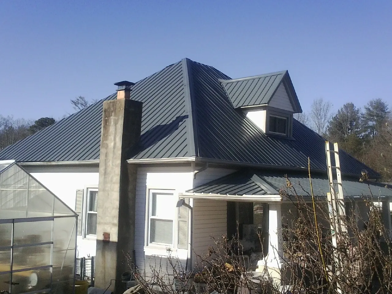 Dark blue standing seam metal roof on a white farmhouse with dormer — Slate & Tile Roof Repair by Roofing Brothers in White Bird
