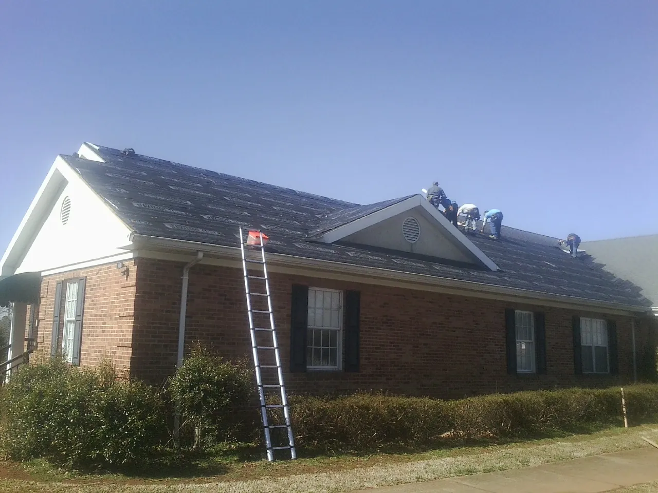 Crew tearing shingles off a brick ranch roof with a ladder set — Emergency Roof Repair work by our crew in White Bird