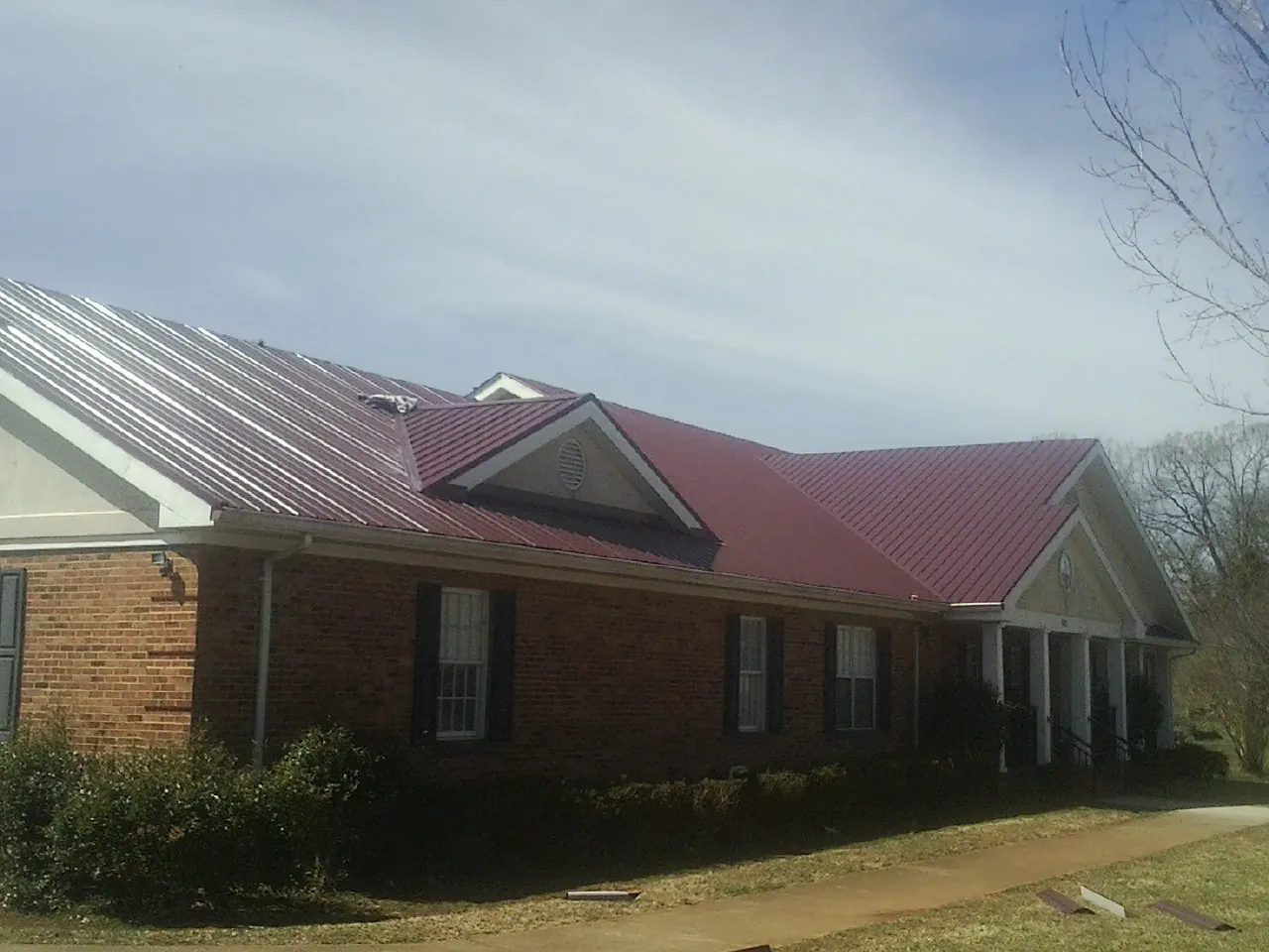 Red metal roof with gabled entries on a long brick building, from a Hail Damage Roof Repair job in White Bird