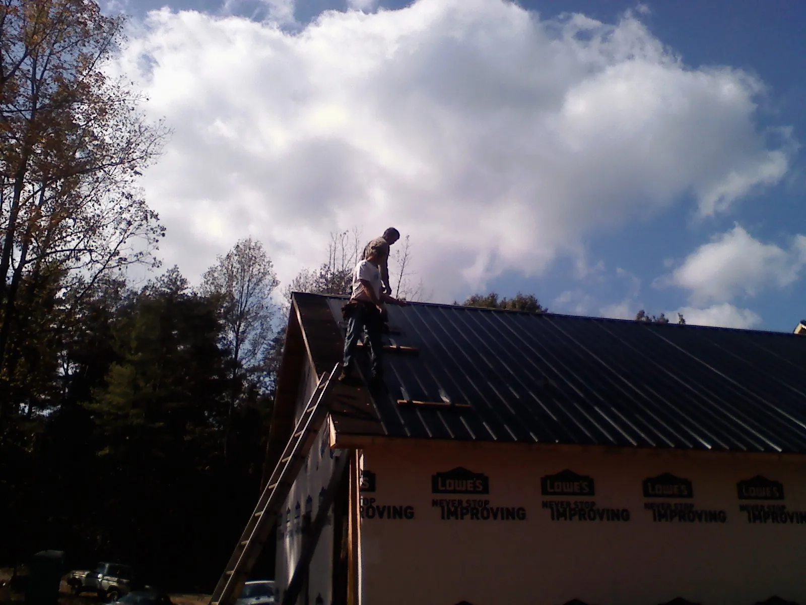 Roofer fastening dark metal panels high against a cloudy sky, from a Roof Inspection job in White Bird