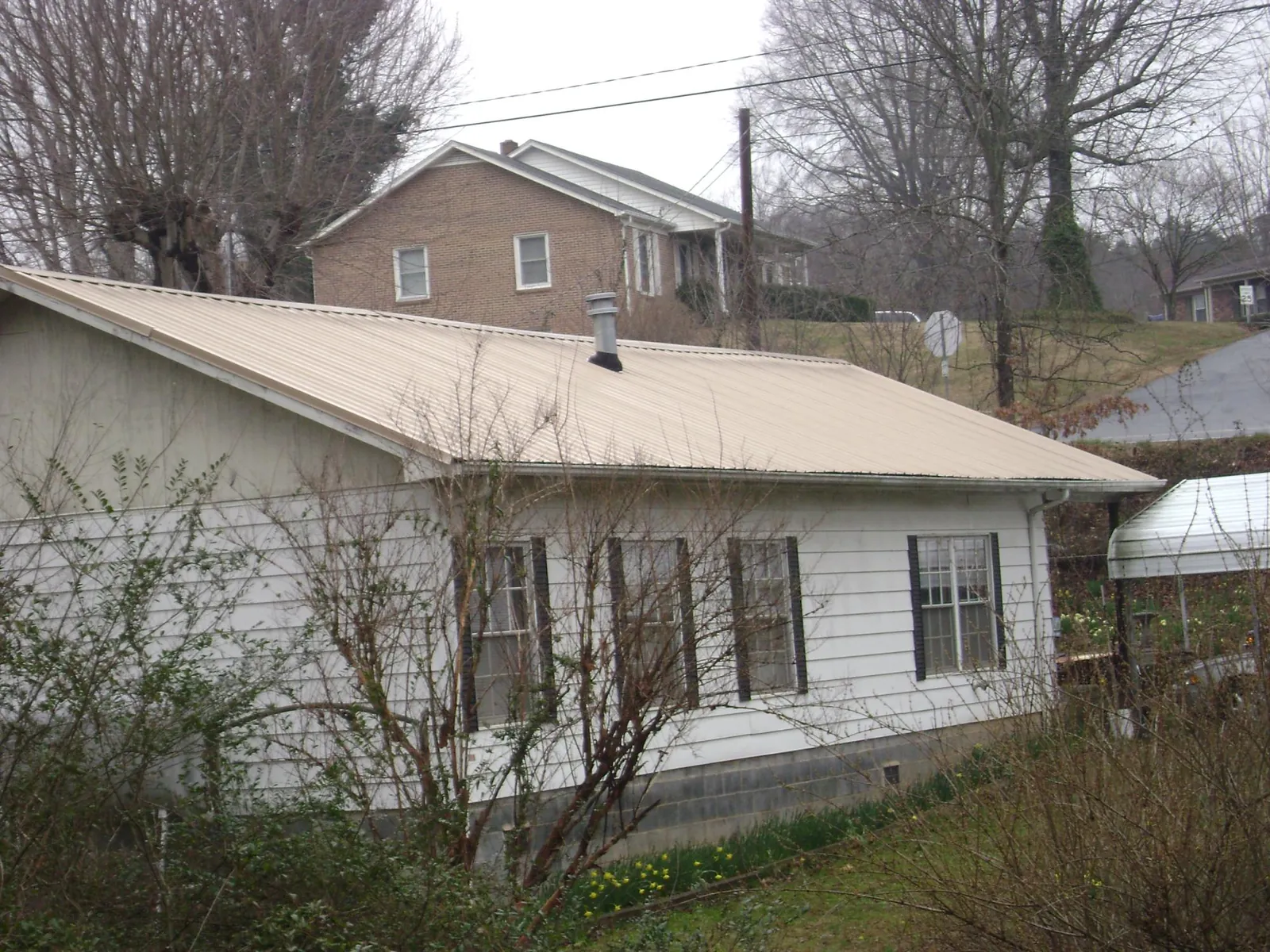 Tan metal roof on a white sided house set into a hillside — Commercial Roofing by Roofing Brothers in White Bird
